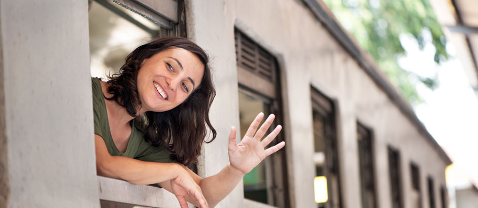 Junge Frau winkt lächelnd aus einem Zugfenster