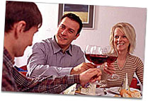 Familie Schneider sitzen mit Nikolaj am Tisch und stoßen mit einem Glas Wein an.